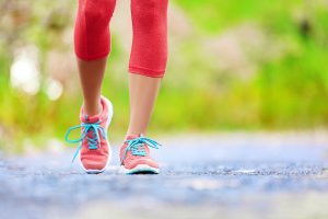 Picture of woman legs running where red workout leggins and red running show with blue shoe laces