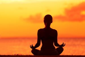 Woman sitting in the sunset doing yoga and meditation