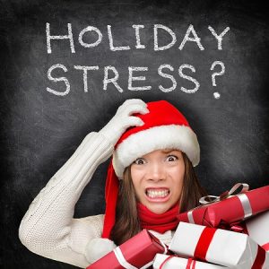 Woman wearing a santa hat with hand gripping head and holding presents. She looks stressed. Text says "Holiday Stress?"