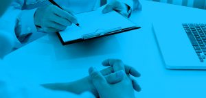 Picture of someone holding a clipboard and pen, a part of labtop, and another persons hands. Image has a blue overlay.