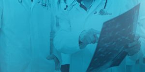 Picture of 2 doctors and one is point to an x-ray. Image has blue overlay.