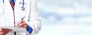 Picture of doctor holding a clipboard and writing. Doctor is also wearing a stethoscope
