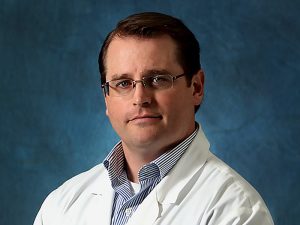Picture of man doctor wearing a white lab coat and blue stripped shirt