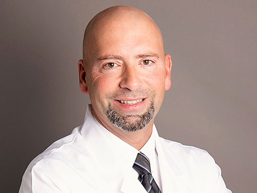 Picture of Neil Billeaud, M.D., in white lab coat and brown, light blue, and navy blue stripped tie